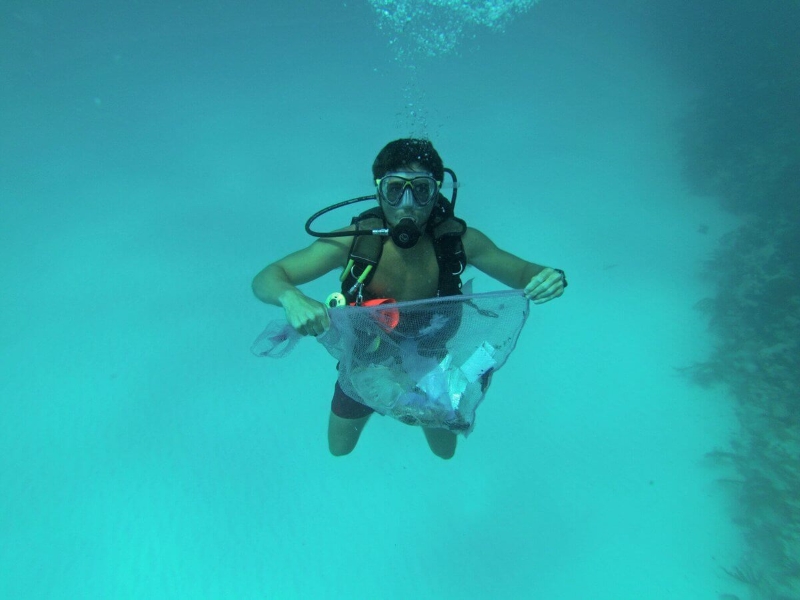un homme sous l'eau avec une bombonne d'oxygène est en train de récolter les déchets dans la mer à l'aide d'une épuisette