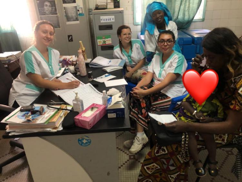 Une équipe de quatre femmes en blouse médicales sourient, assise face à elles une femme avec son bébé (visage caché par un emoji coeur) sur les genoux