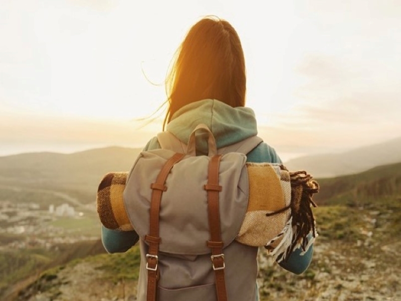 Une femme avec un backpack regarde un horizon, paysage de montagnes au coucher de soleil