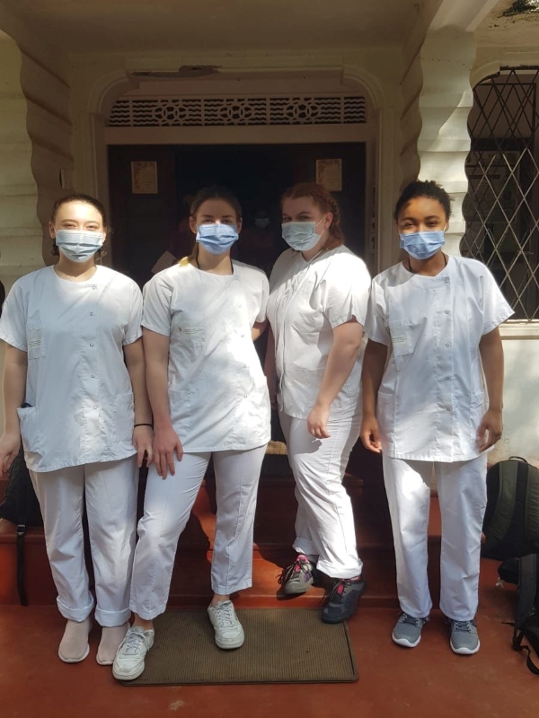 Quatre jeunes bénévoles sont en tenues médicales et masquées et sourient face à la caméra.